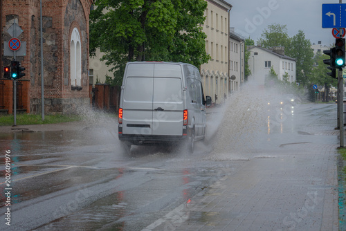 Delivery van driving through flooded urban street during heavy rain and severe weather