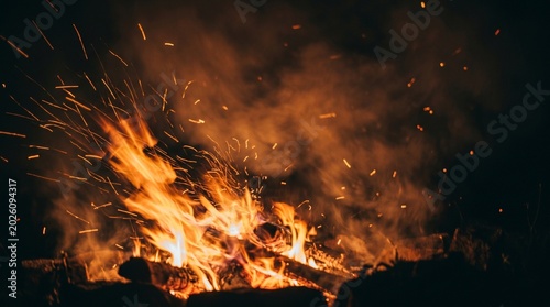 Tablou pe pânză Abstract background of vibrant bonfire flames with glowing sparks and smoke rising in the dark