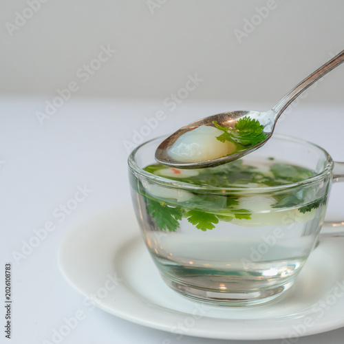 Glass mug of clear liquid with fresh herbs and ice, a spoon lifts a piece of herb
