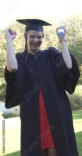 Vertical video: Female graduate after ceremony cheering, raising diploma and pumping on quad in cap