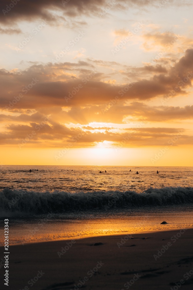 Obraz premium Dramatic golden sunset with sun rays over Pacific Ocean and surfer silhouettes