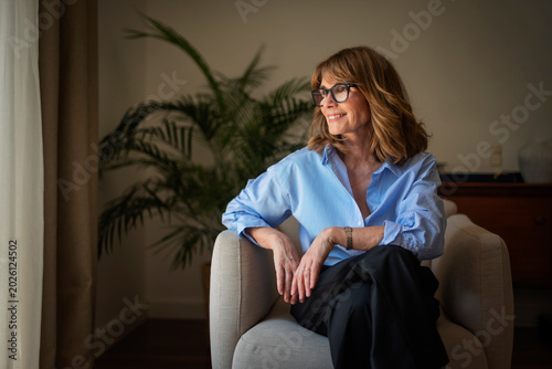 Bild auf Leinwand Portrait of a stylish mid aged woman sitting in an armchair in a minimalist home