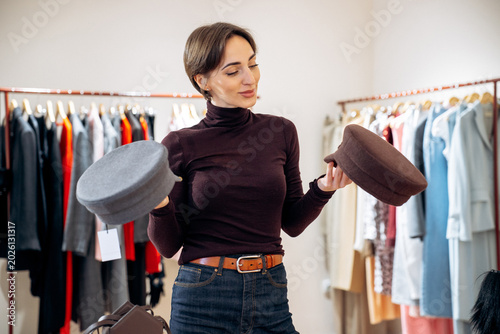 Fotografie Woman standing in a boutique choosing between two stylish hats, enjoying the sho