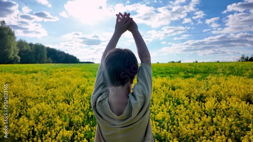Slow motion video of boy raising hands in yellow rapeseed field under sunny blue sky. Nature, freedom and childhood lifestyle concept