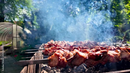 Close up of juicy meat skewers grilling on charcoal brazier with smoke and glowing coals in sunny outdoor backyard