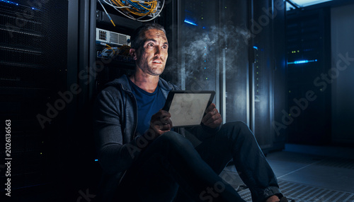 IT specialist sits on the floor of a dark server room while dealing with a data center crash