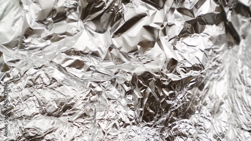 Crumpled aluminum foil surface moving and reflecting light. Abstract metallic texture background footage with shiny wrinkles and folds. Industrial material and packaging concept for design, wallpaper 