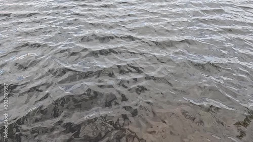 Grey natural water surface filmed at low wide angle in slow motion shows steady small ripples continuously moving across frame under overcast diffused daylight outdoors
