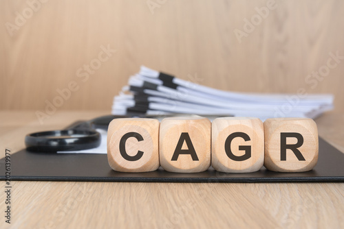 CAGR concept with wooden blocks, financial documents and magnifying glass on office desk