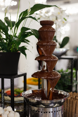 Elegant chocolate fountain at a restaurant event with flowing milk chocolate on a luxury dessert buffet. Perfect for themes related to catering, weddings, celebrations, sweet tables, gourmet desserts,