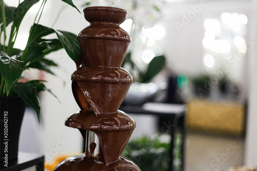Elegant chocolate fountain at a restaurant event with flowing milk chocolate on a luxury dessert buffet. Perfect for themes related to catering, weddings, celebrations, sweet tables, gourmet desserts,