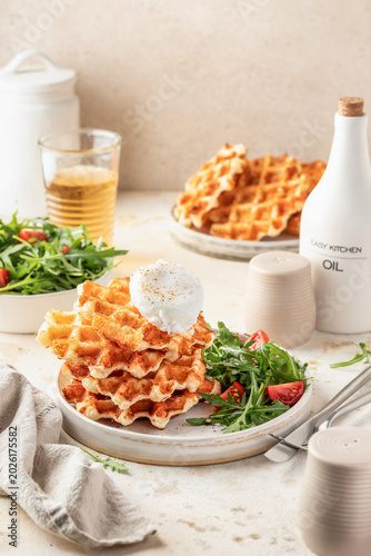 Savory cheesy waffles with poached egg and green arugula tomatoes salad, healthy morning vegetarian breakfast on beige table background