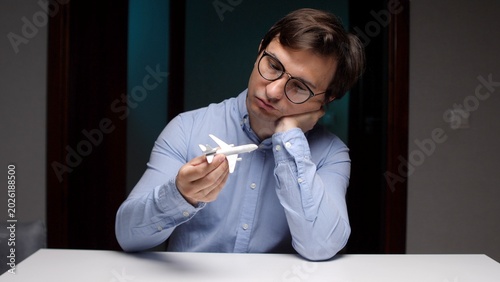 Fotografía Young man wearing glasses holding a small toy airplane, resting his head on his