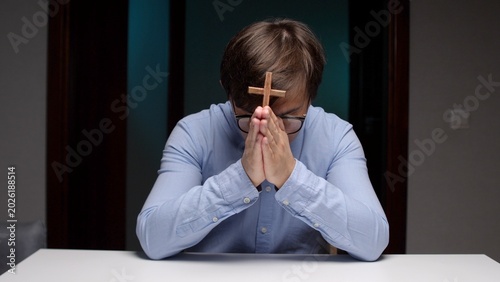 Canvas Print Man holding a wooden cross on his forehead with hands clasped in prayer, express