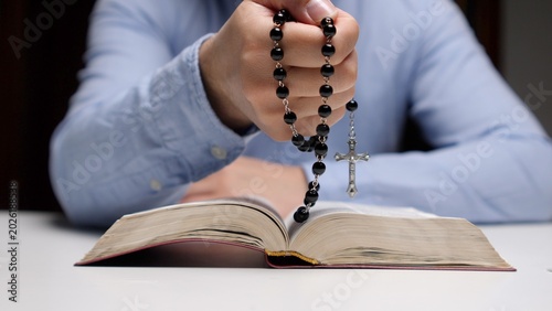 фотографія Hand holding rosary beads with crucifix over open bible, close up evoking faith,