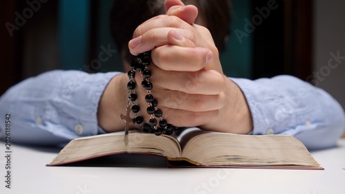 Foto Person with clasped hands holding a rosary with a cross while kneeling or leanin