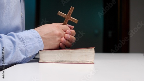 Tableau sur toile Person's hands clasped together in prayer, holding a wooden cross over an open s