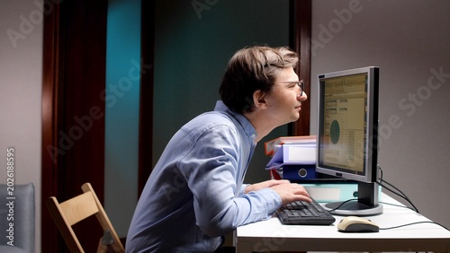Tablou pe pânză Man with glasses hunches over a computer screen, diligently typing on the keyboa