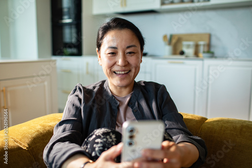 Smiling woman using smartphone at home on sofa