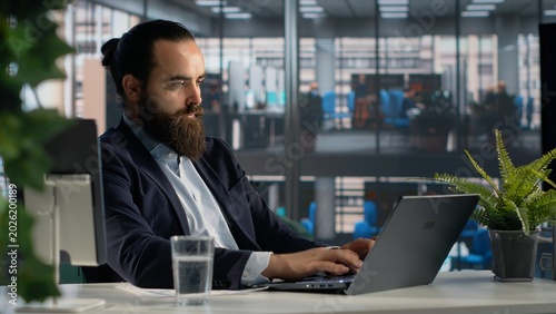 Foto Business owner in corporate office reviewing documents, planning new growth strategy on laptop with support from company data