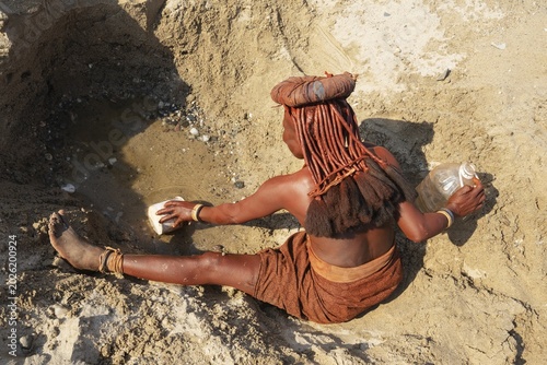 Himba woman collecting water at a water hole, at the bank of the dry river bed of the Hoarusib river, Kaokoland, Kunene Region, Namibia