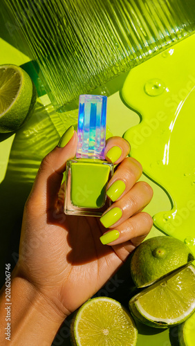 Hand holding lime green nail polish bottle on a vibrant citrus background.