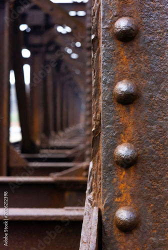 Rusty iron beam with rivets of old bridge. Industrial city structure background for wallpaper. Close up texture of weathered metal girder repeating in perspective for urban design.