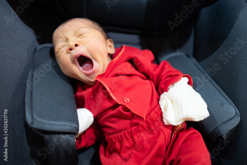Yawning Newborn Baby in Red Outfit Lying in Car Seat