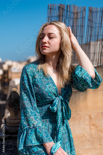 Young woman poses outdoors in a blue dress while enjoying warm sunlight on a clear day