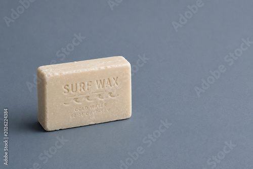 A single surf wax block placed on a matte ocean gray-blue background creates a modern surfing culture atmosphere.