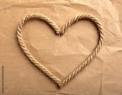 Heart shape made of rustic jute rope on textured brown kraft paper, symbol of love and romance, rustic wedding invitation element