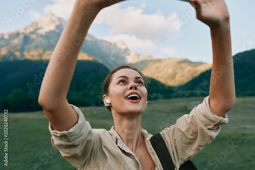 Fotografie Joyful brunette woman raises her arms in a sunlit mountainside meadow, capturing a moment of outdoor adventure, freedom, and positive energy in the open air