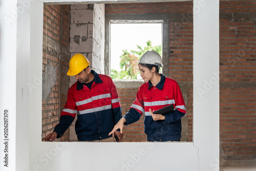 Slika na platnu Professional engineers wearing hardhats inspecting unfinished brick wall structu