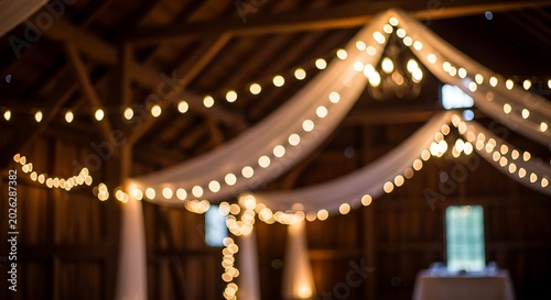 String lights and draped fabric illuminate a rustic wooden barn interior creating a warm and inviting atmosphere for an event or celebration.