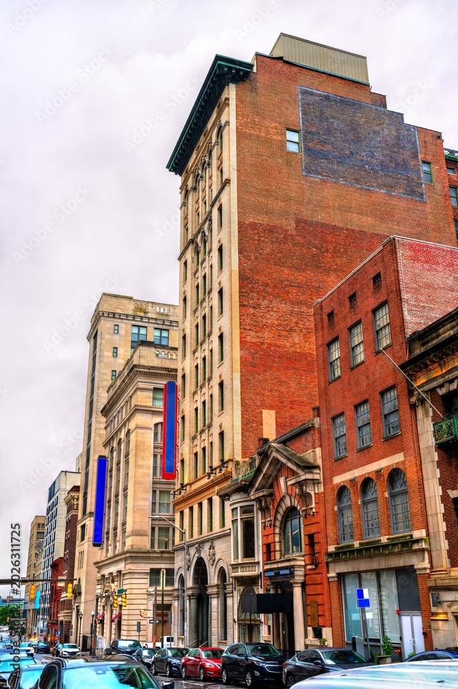 Obraz premium A view of historic architecture along Calvert Street in downtown Baltimore, Maryland, United States. The scene features a mix of brick and stone commercial buildings on an overcast day