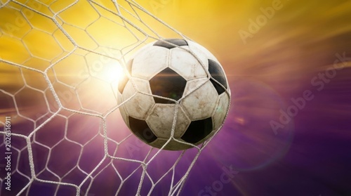 Soccer ball flying into goal net at sunset