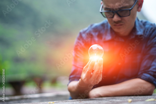 Man Holding Glowing Light Bulb Against Green Nature Background