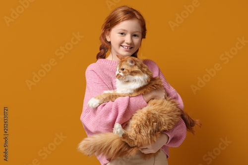 Redhead teenage girl with cute cat on orange background