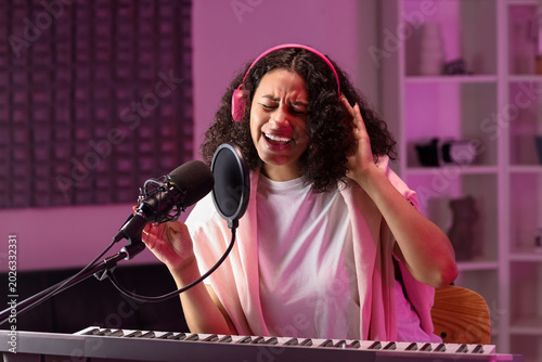Foto Young African-American woman with headphones and microphone singing in recording