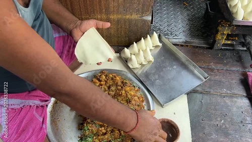 A skilled local cook frying fresh handmade samosas at a traditional roadside tea stall, surrounded by aromatic Indian spices in a busy street of Kolkata.