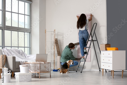 Foto Young couple with Beagle dog wallpapering during repair in their new house