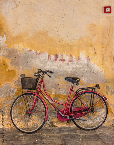 A red bicycle with a wicker basket leaning against an orange wall