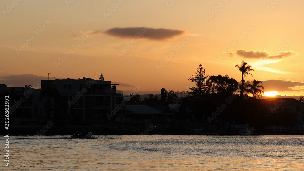 Fototapeta premium Sunset Over Silhouetted Waterfront Homes and Palm Trees by the Water