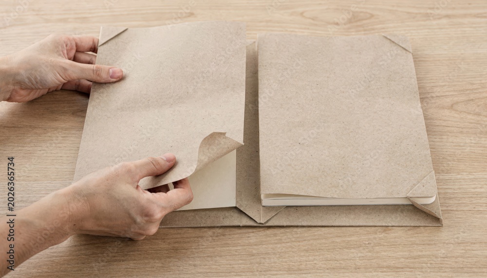 Obraz premium Medium shot focusing on assembling a card wrap cover for a layflat notebook highlighting folding techniques and protective corner shaping on a wooden table.