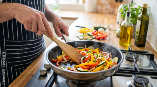 Foto Person cooking fresh vegetables in a frying pan on a stovetop.