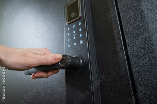 Obraz na plátně A woman opens a modern smart door lock with a digital keypad and biometric fingerprint access
