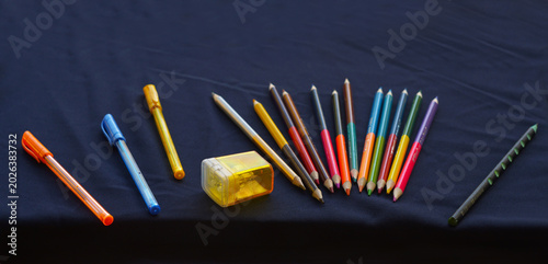 Billede på lærred Colorful stationery set with pencils, pens, and a sharpener on a dark background