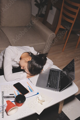 Exhausted female employee experiencing burnout while working overtime. A tired professional woman under pressure with a headache.