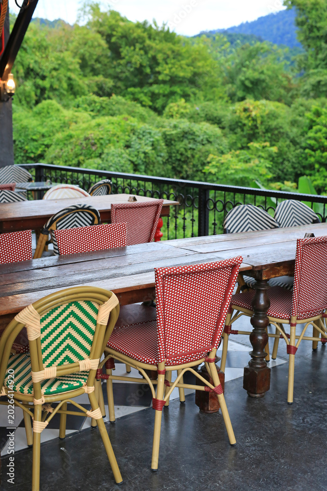 Obraz premium Empty bistro tables and woven chairs sit quietly on a balcony, waiting for guests to enjoy a meal overlooking the lush tropical forest and distant mountains.