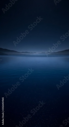 Serene, dark blue lake at twilight with misty hills